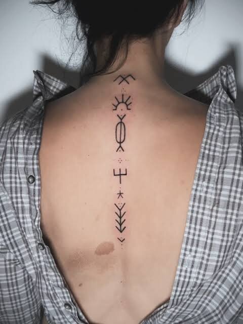 a line of deq signs tattooed down a woman's spine